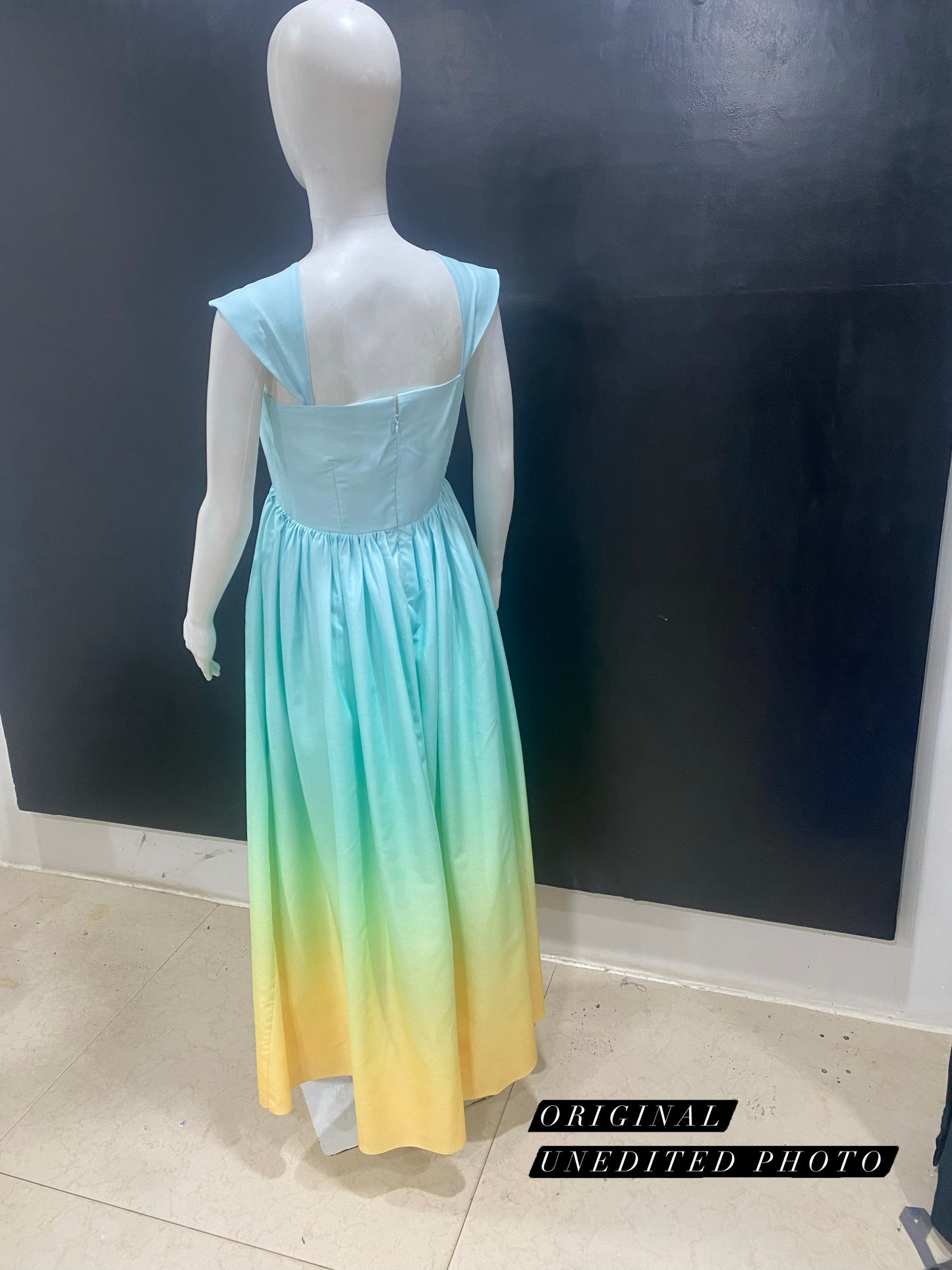 Mannequin wearing a gradient dress from blue to yellow against a dark wall.