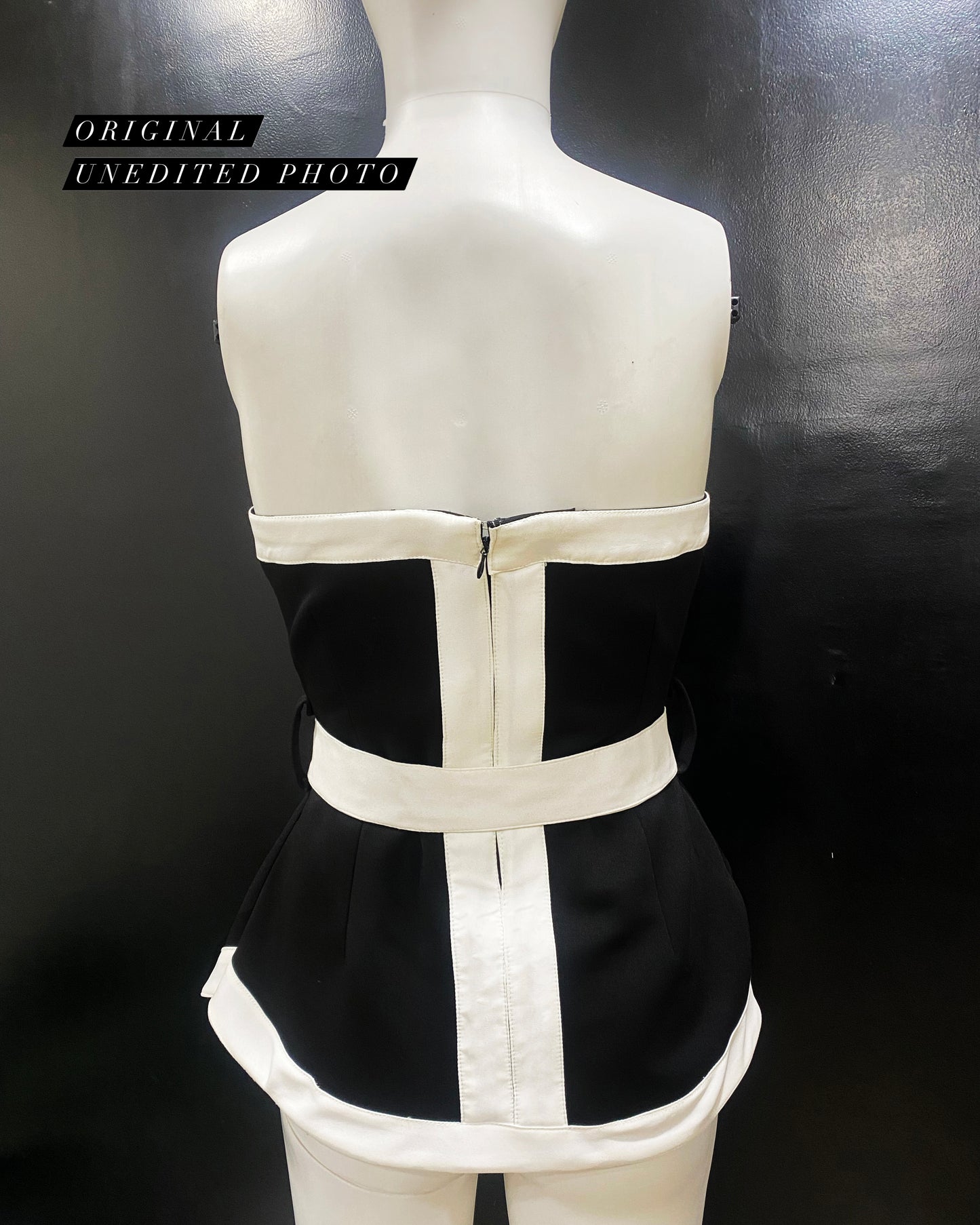 A mannequin torso showcasing a white and black asymmetric strapless top with white accented panels and a cinched waist bow belt.