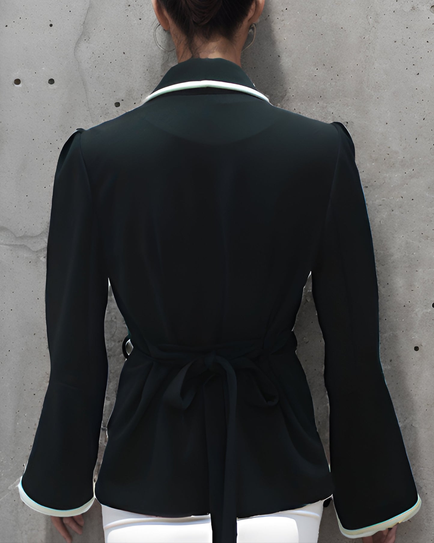 Person wearing a black coat with white trim against a concrete wall.
