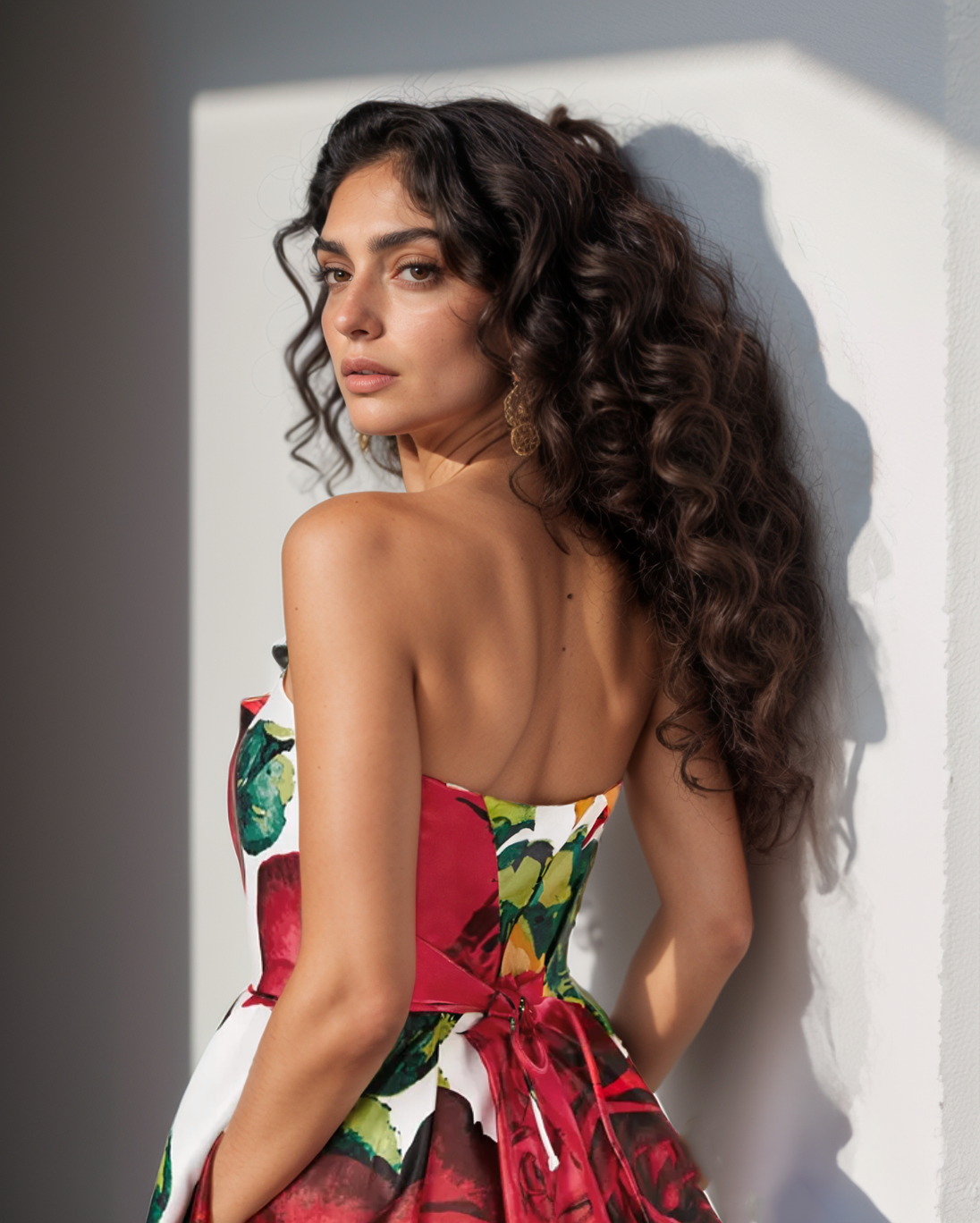 Woman wearing a colorful dress with floral patterns, standing against a neutral background.