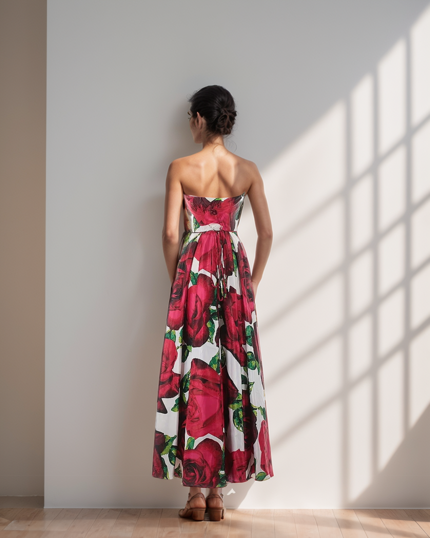 Woman wearing a strapless floral dress standing in a sunlit room.