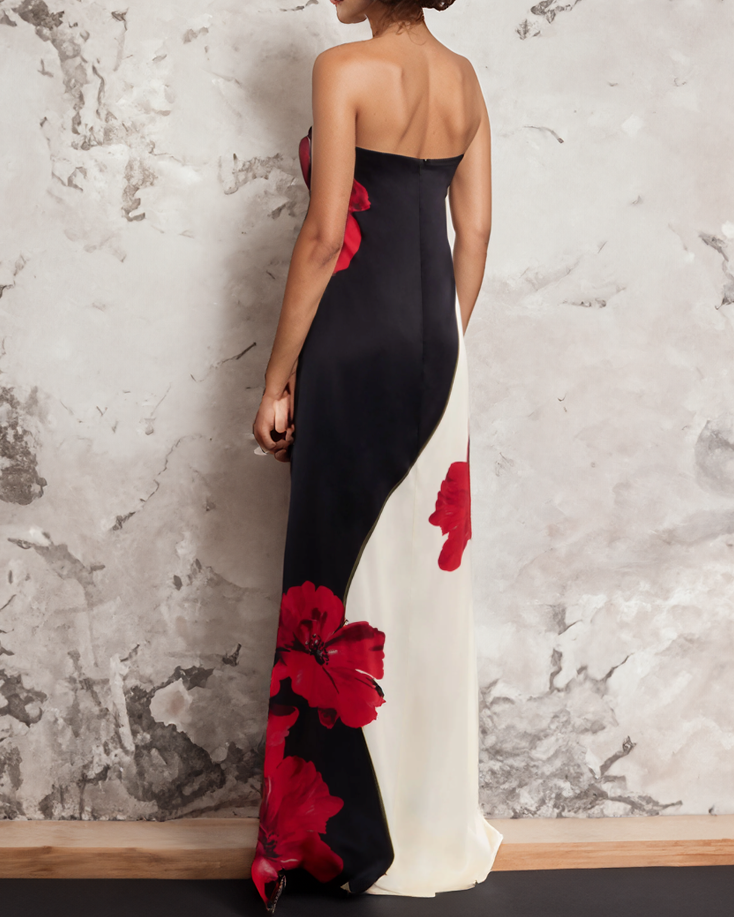 Black strapless gown with red floral accents against a textured wall.
