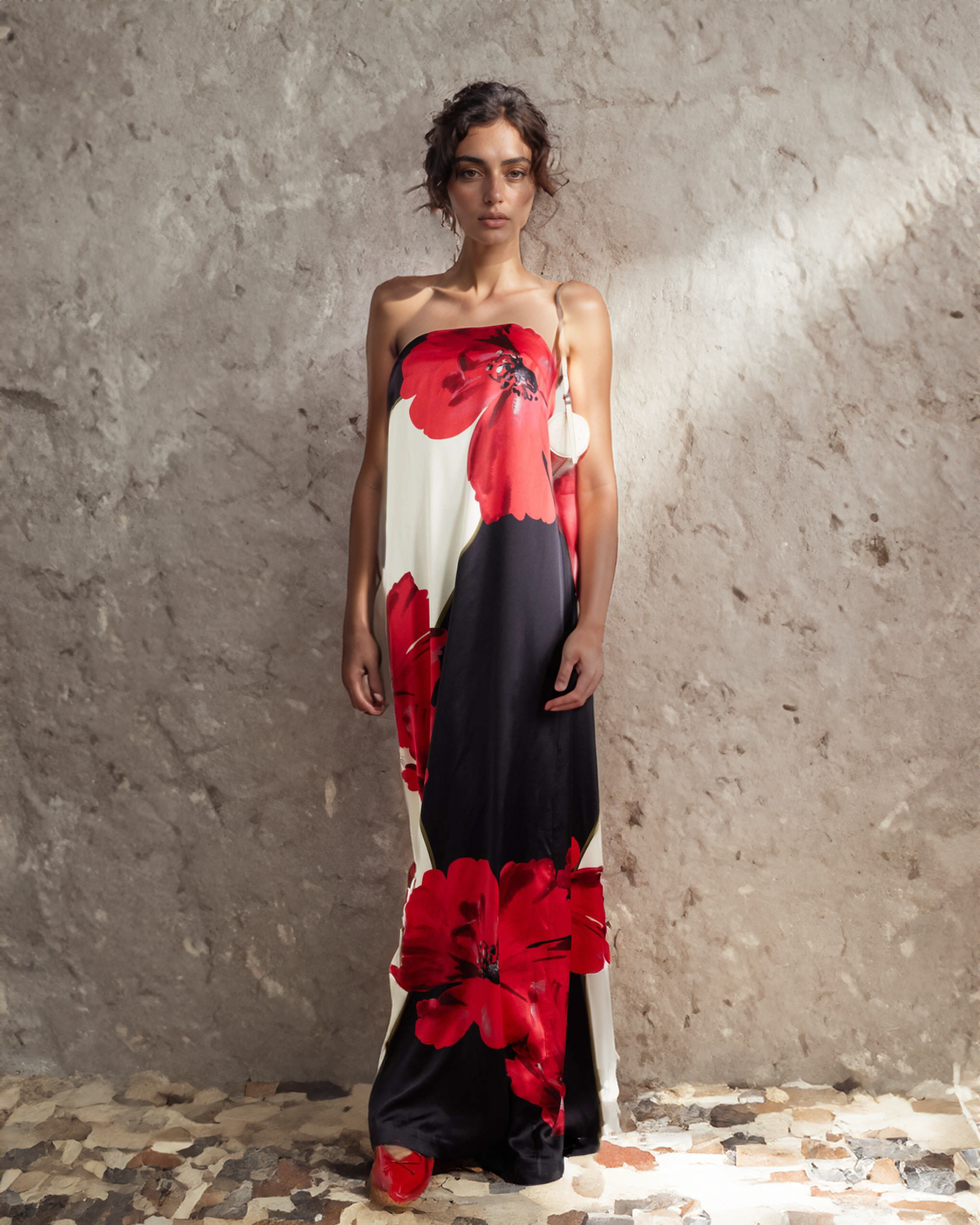 Model wearing a strapless dress with red floral patterns against a textured wall.