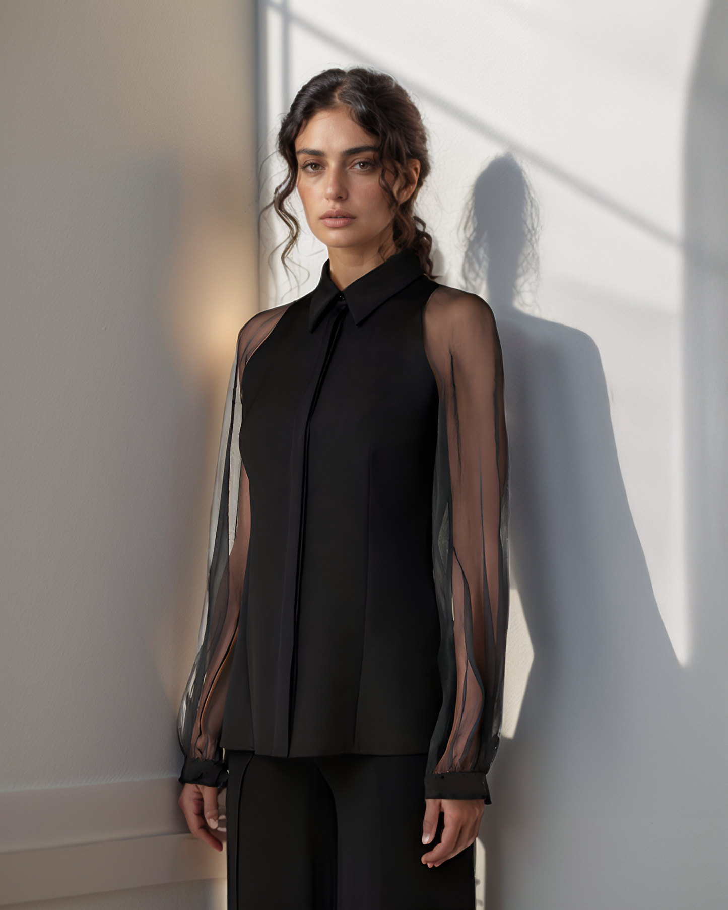 Woman wearing a black sheer blouse over a black shirt with a plain background