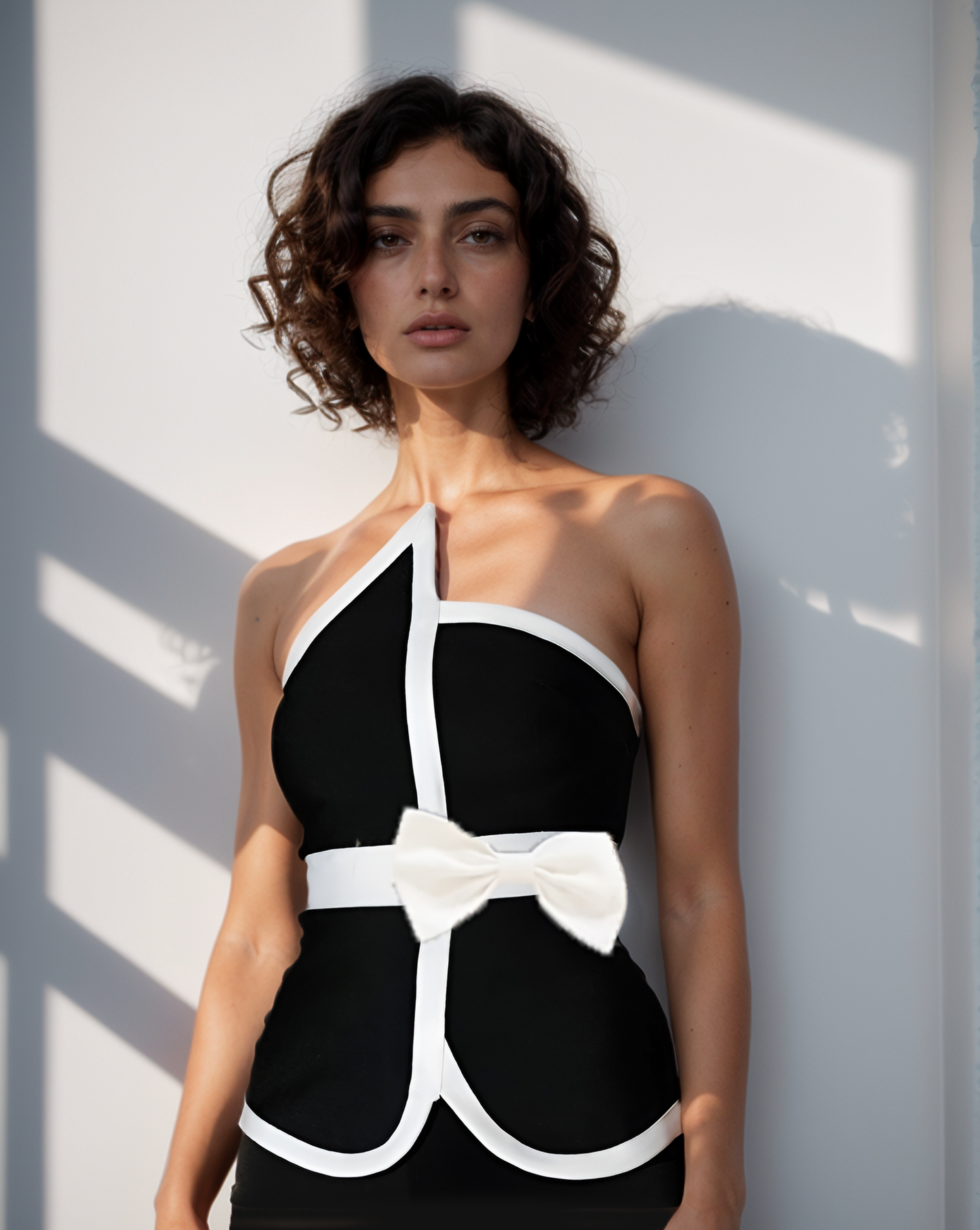 Woman wearing a black and white dress with a bow detail against a light background