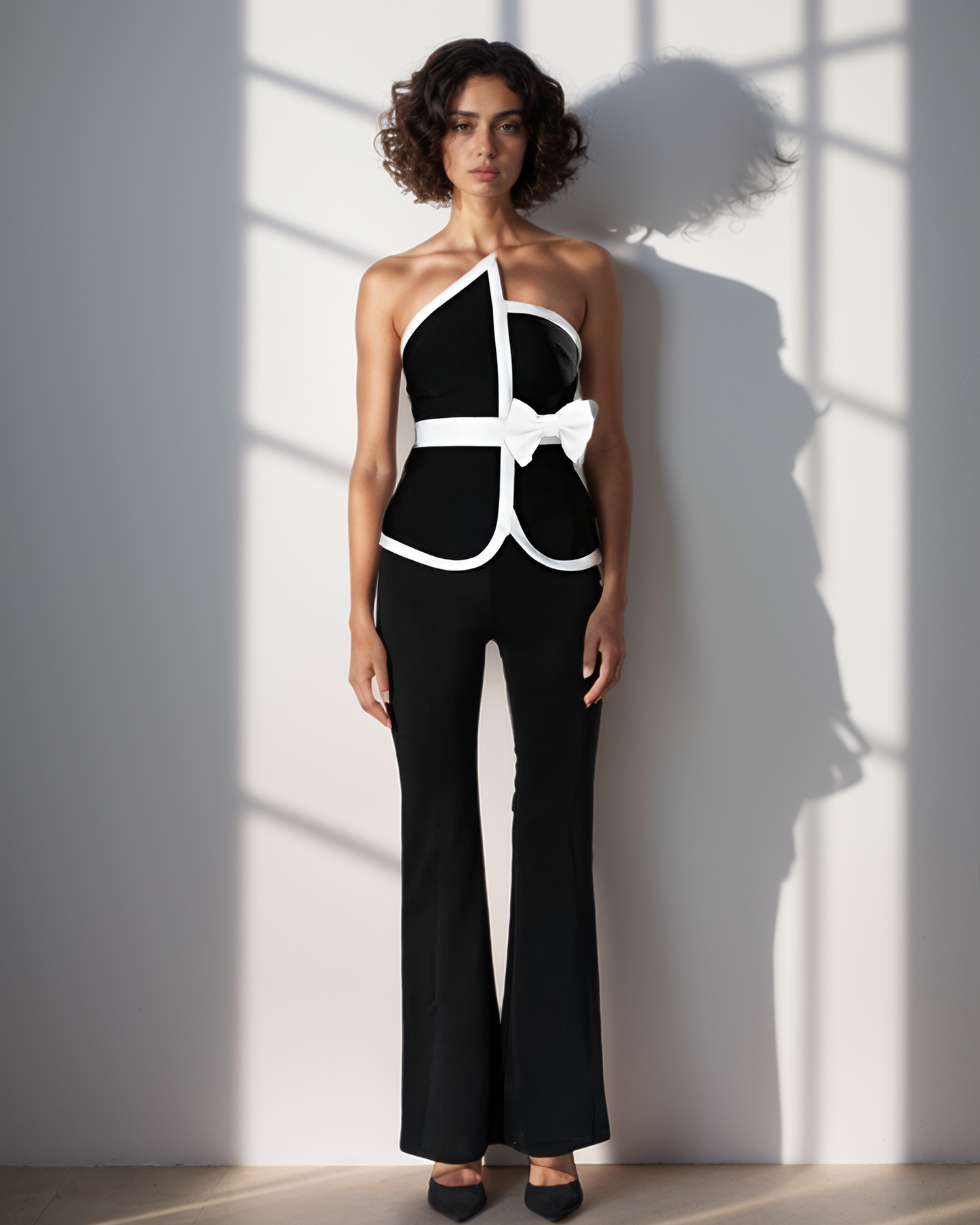 Woman wearing a black and white outfit standing against a light gray wall with shadows.