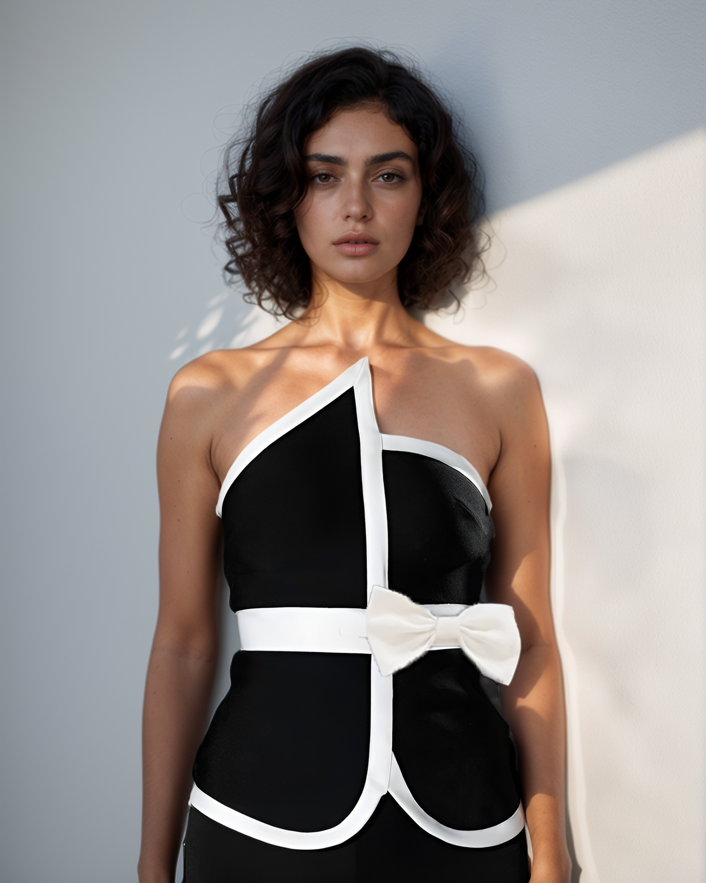 Woman wearing a black and white dress with a bow detail against a light gray background