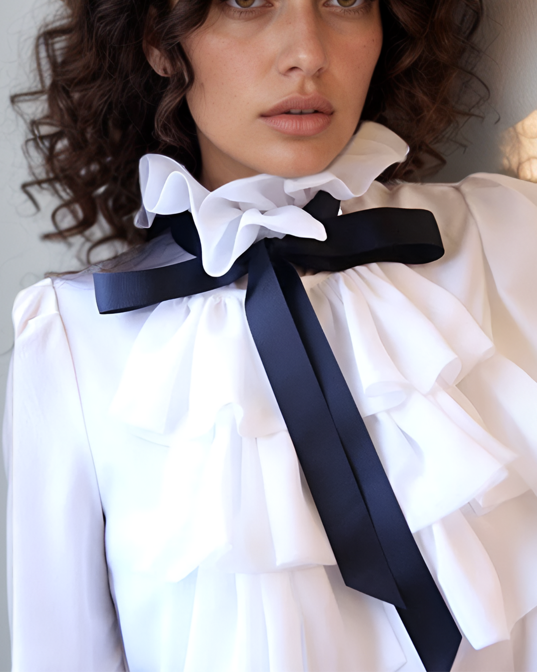Woman wearing a white blouse with a large black bow tie against a neutral background