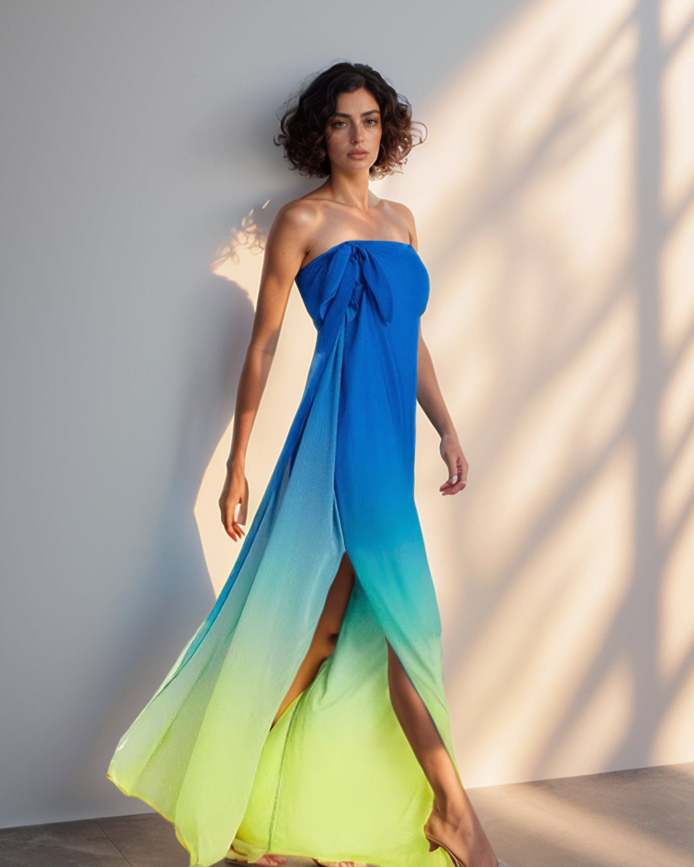 Woman wearing a strapless, floor-length dress with a gradient of blue to green against a neutral background.