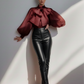 Person wearing a burgundy top with large bow and black leather pants against a white wall.