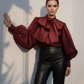 Woman wearing a burgundy blouse with ruffled details and black leather pants against a light background