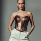 Model wearing a metallic bronze corset top and light-colored pants against a gray background