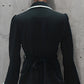 Person wearing a black coat with white trim against a concrete wall.