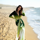 Woman in a green and black dress standing on a beach
