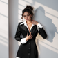 A woman wearing a black blazer shirt dress with white accents, featuring a sharp shirt collar and shirt cuffs.