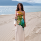 Woman in a colorful dress standing on a sandy beach with mountains and ocean in the background