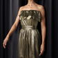A woman wearing a gold metallic strapless dress with a double-ruffled neckline and a metallic tie-belt.
