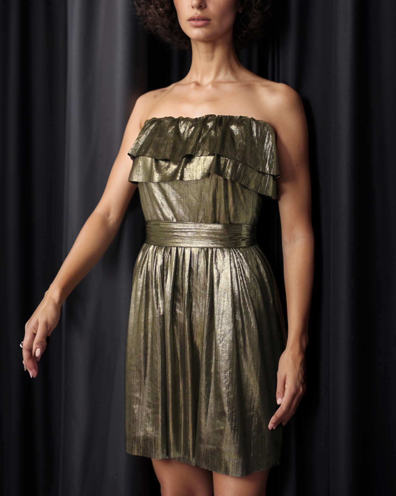 A woman wearing a gold metallic strapless dress with a double-ruffled neckline and a metallic tie-belt.