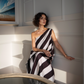 Woman in a black and white striped dress standing against a white wall.