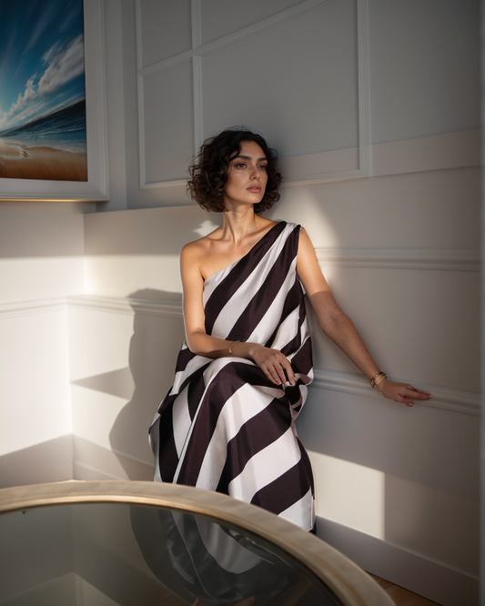 Woman in a black and white striped dress standing against a white wall.
