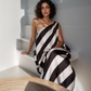 Woman wearing a black and white striped dress sitting on a white wall.