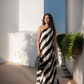 Woman in a black and white striped dress standing against a white wall with a blue sky.