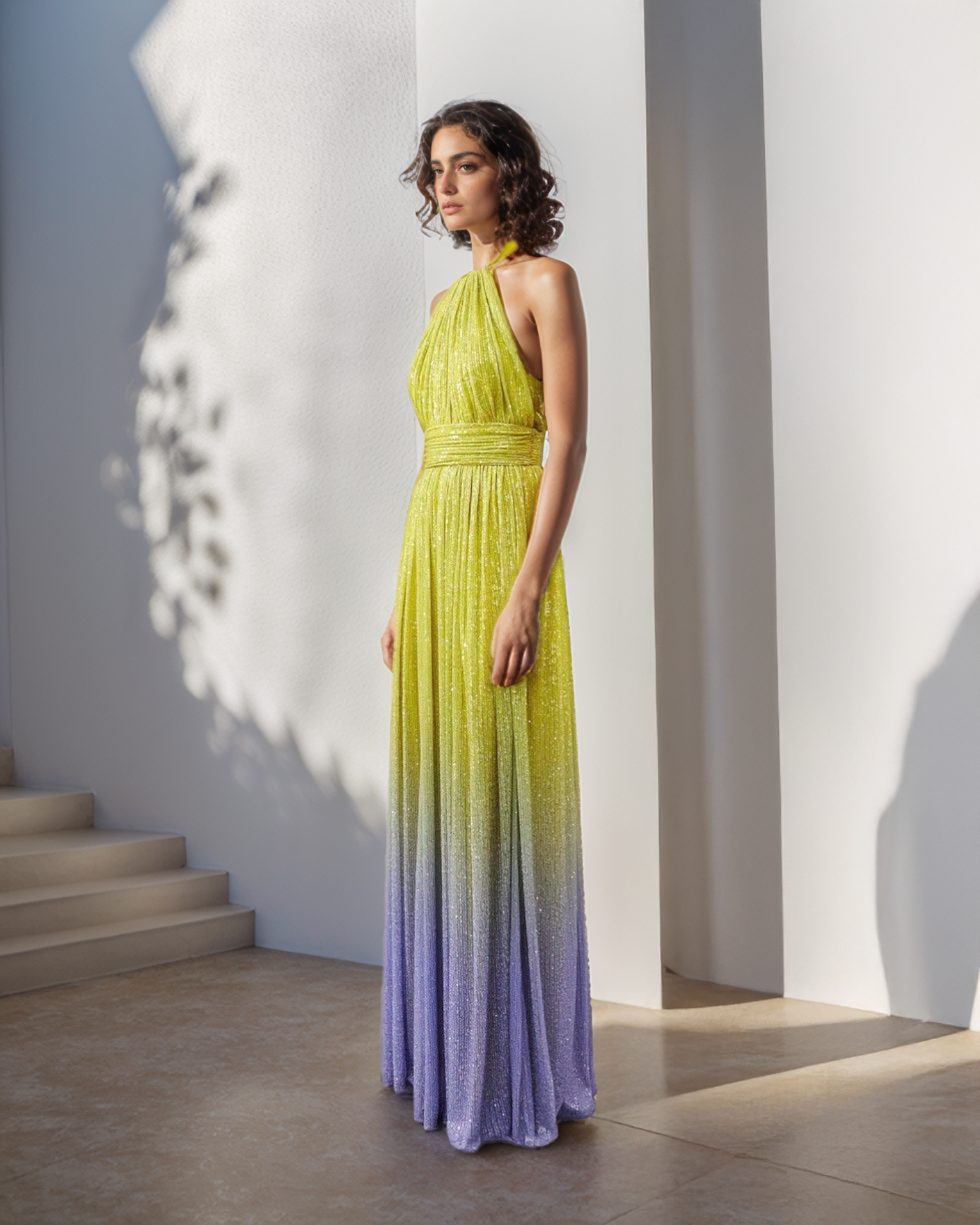 Woman wearing a gradient dress standing in a sunlit room with white walls and steps.