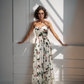 Woman wearing a rose floral strapless dress standing against a white wall with sunlight casting shadows.