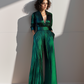 Woman wearing a green jumpsuit standing against a white wall with sunlight casting shadows.