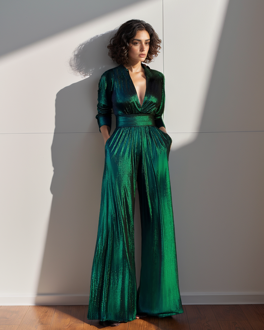 Woman wearing a green jumpsuit standing against a white wall with sunlight casting shadows.