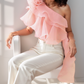 Woman wearing a pink one-shoulder top and white pants sitting on a chair.