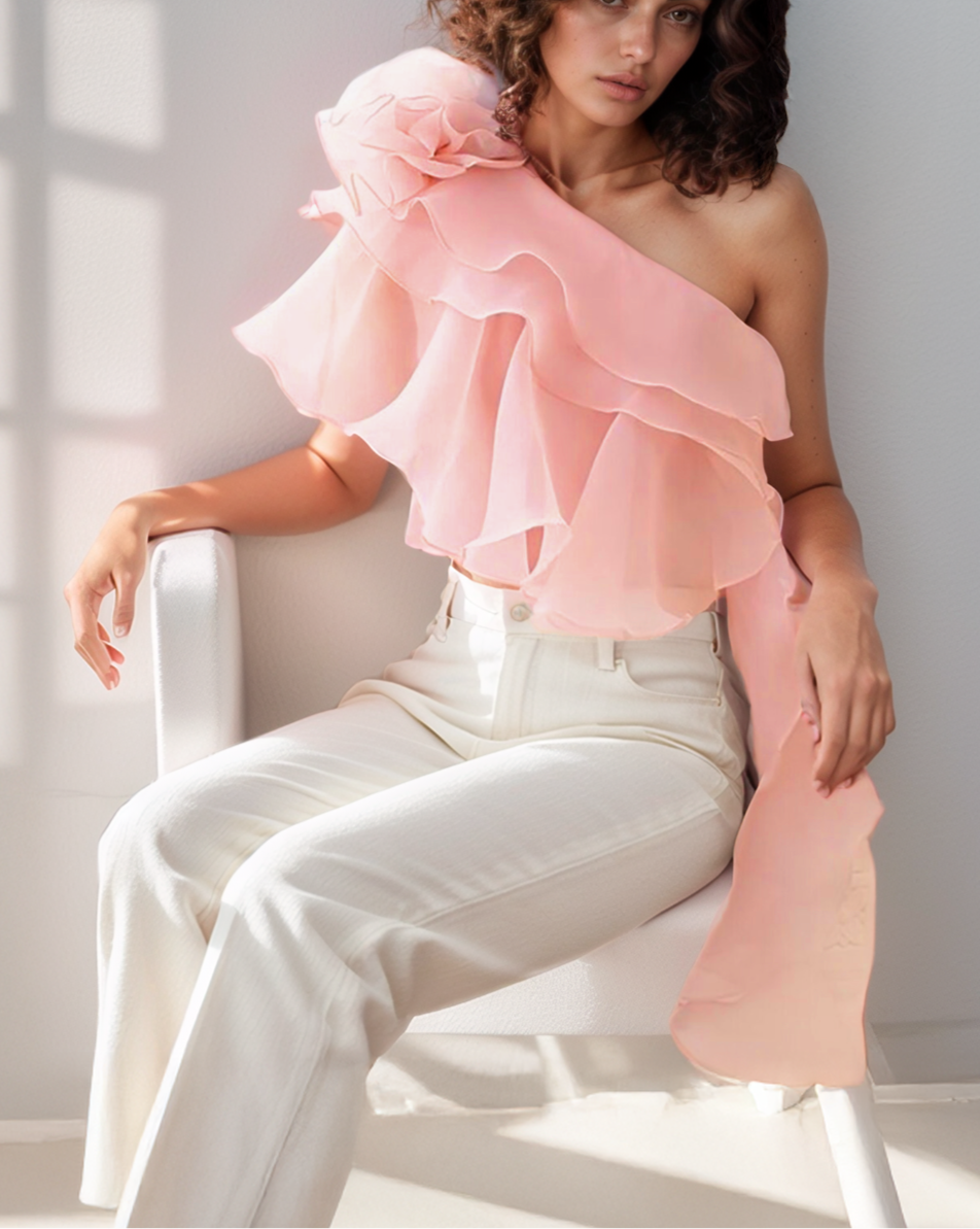 Woman wearing a pink one-shoulder top and white pants sitting on a chair.
