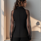 Woman wearing a black outfit with sheer sleeves against a light wall.