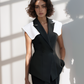 Woman in a black and white outfit standing in a sunlit room with shadows on the wall.