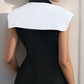 Woman wearing a black dress with a white collar against a light wall.