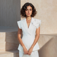 Woman in a white outfit holding a white handbag against a beige wall.