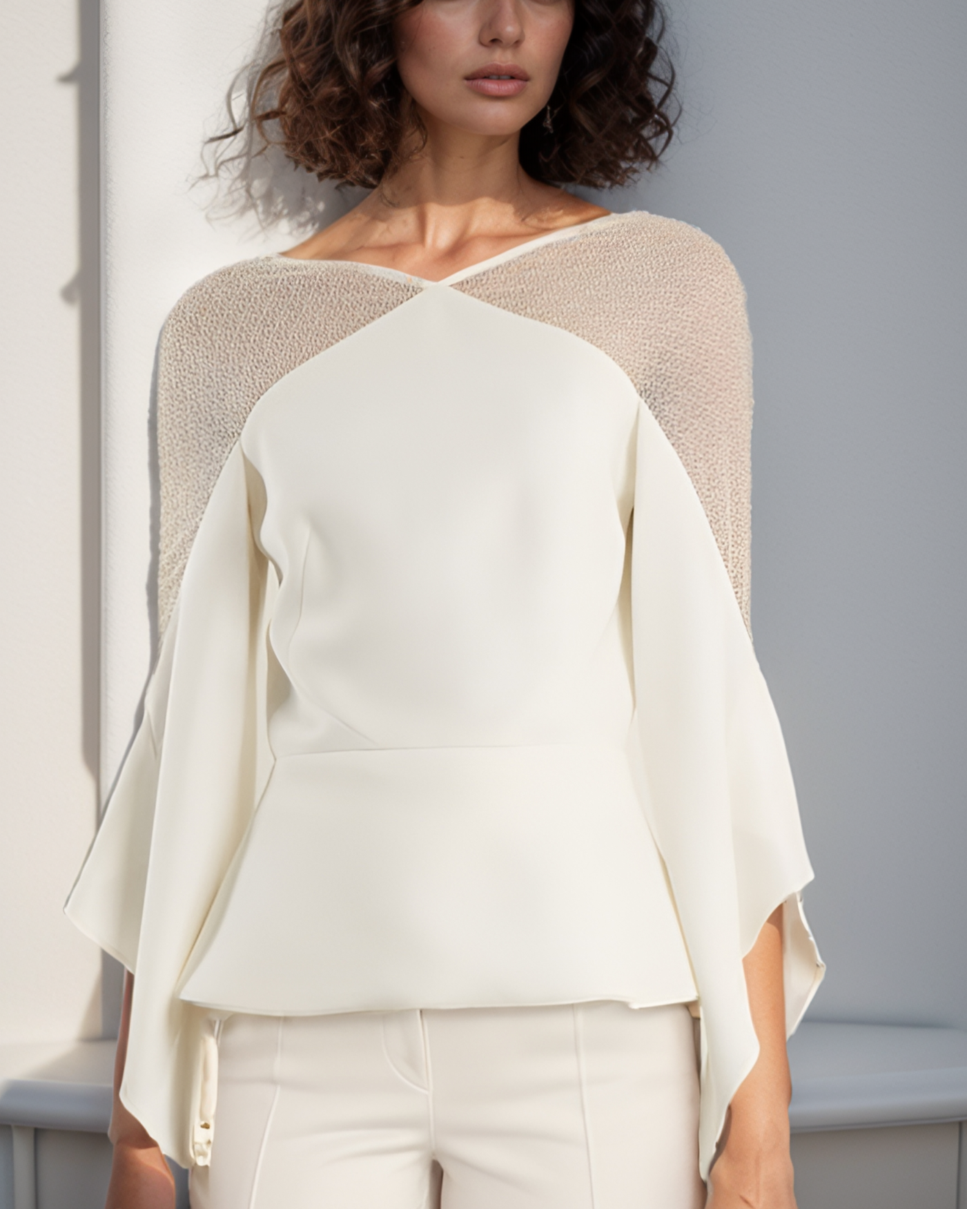 Woman wearing a stylish outfit with a beige top and white pants against a neutral background