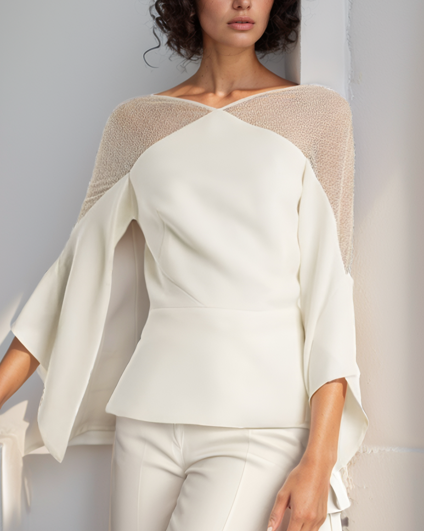 Woman wearing a cream-colored outfit with a light beige cardigan against a neutral background