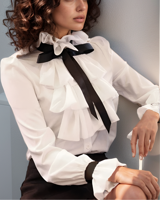 Woman wearing a white blouse with black ribbons against a gray background