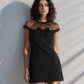 Woman in a black dress standing against a white wall with shadows.