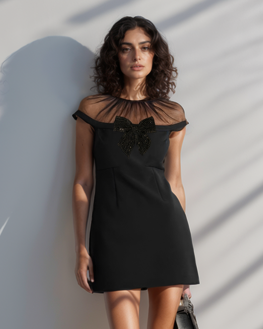 Woman in a black dress standing against a white wall with shadows.