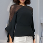 Woman wearing a black top with sheer sleeves against a light gray wall.