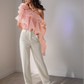 Woman wearing a pink ruffled top and white pants against a plain background