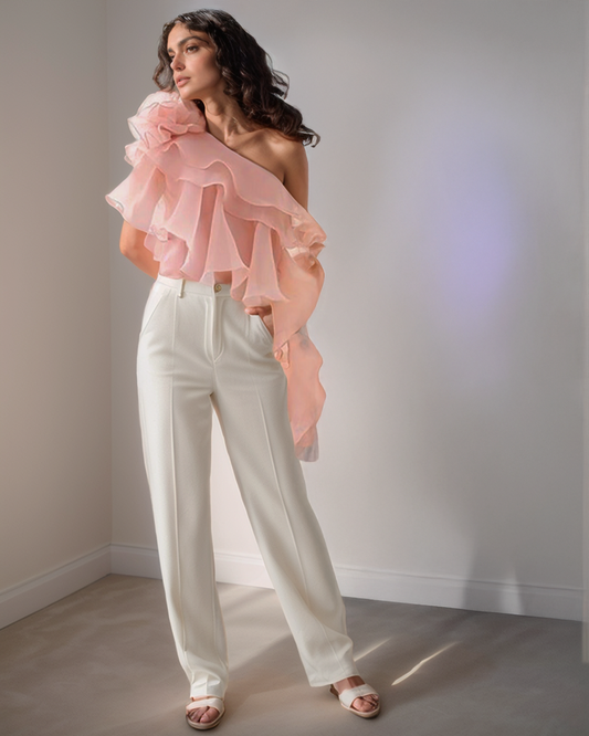 Woman wearing a pink ruffled top and white pants against a plain background