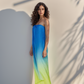 Woman wearing a gradient dress standing against a neutral wall with shadow patterns.