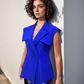 Woman wearing a bright blue sleeveless top against a light wall.