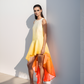 Woman wearing a gradient dress from yellow to orange against a white wall.