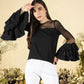 A woman modeling a black top with sequined ruffle sleeves and a round neckline, paired with white pants.